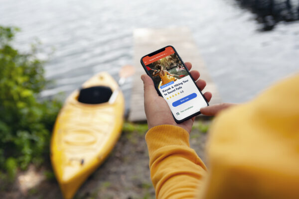 The tourist holds a phone in his hands. Mock up smartphone close-up on the background of a kayak and a lake. Concept on the topic of tourism and recreation